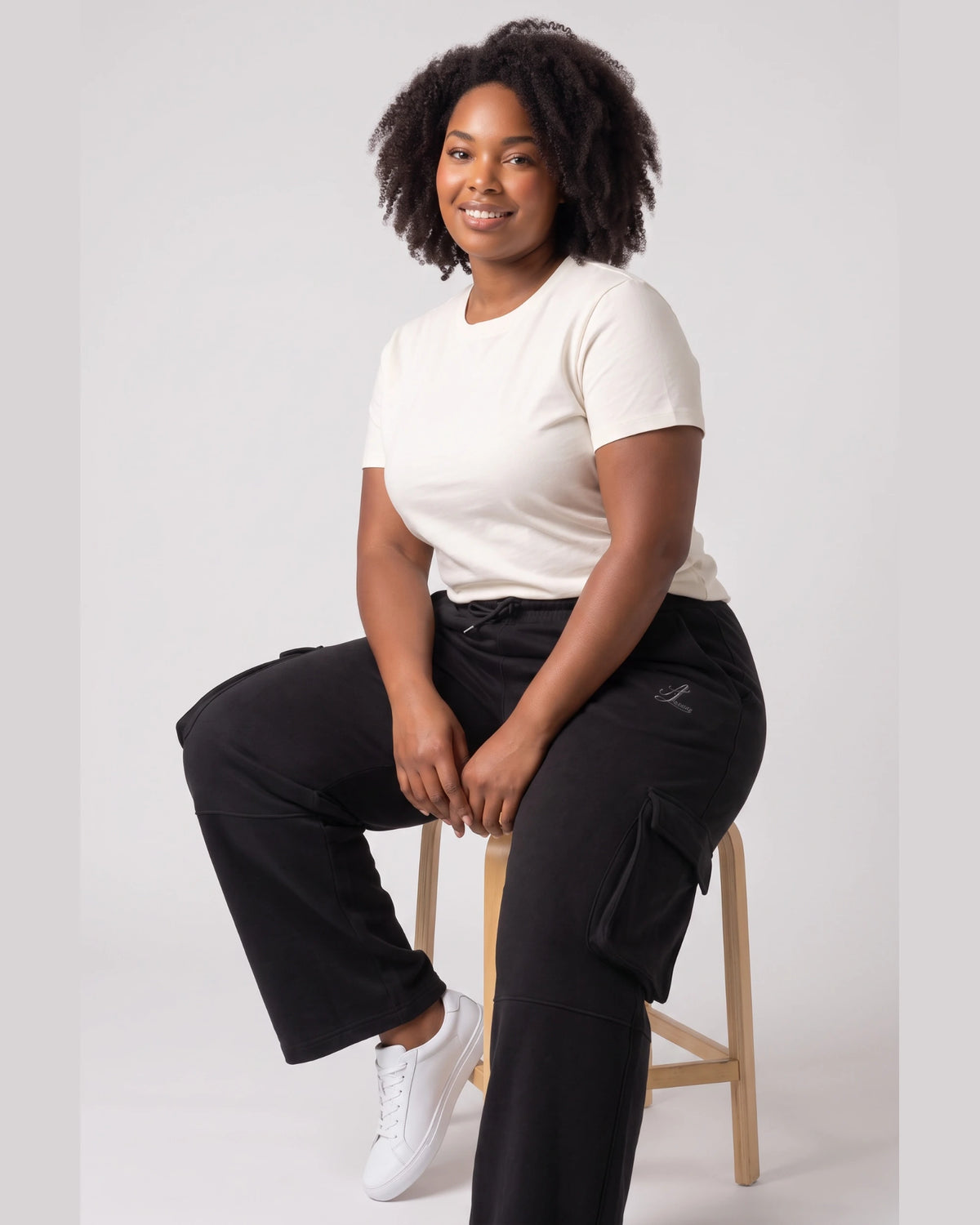 Woman seated wearing black Legacy heavyweight organic cotton cargo pants with thigh flap pockets.