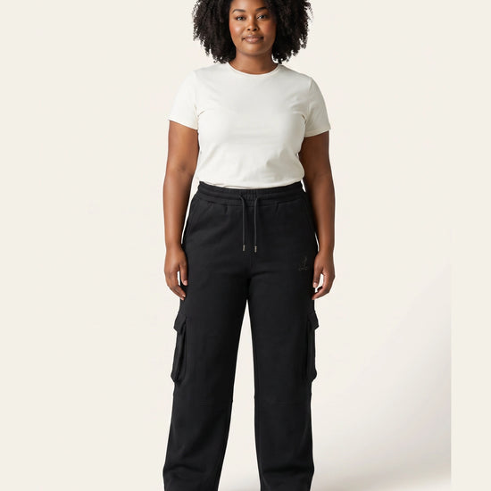 Front view of woman wearing black Legacy 450 GSM cargo pants with elastic drawcord waist and utility pockets.