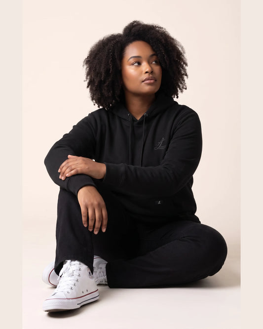 Woman seated in black Legacy organic cotton hoodie and matching trousers.