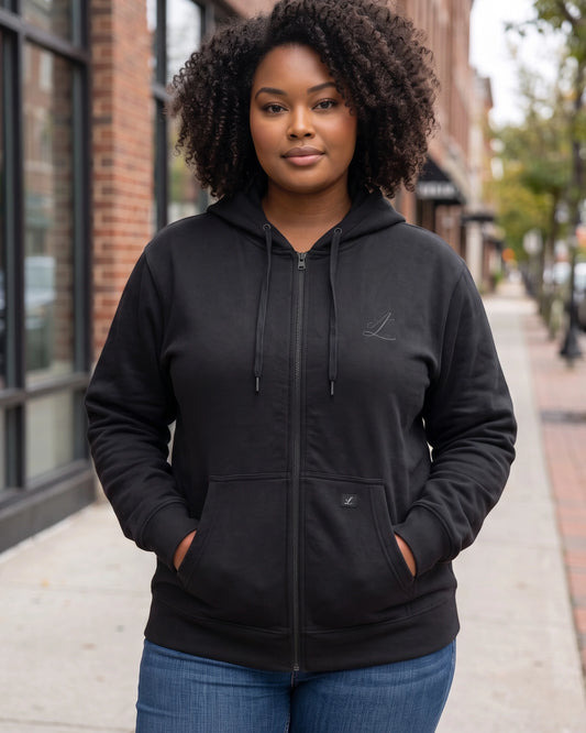Woman wearing the Legacy black zip hoodie with braids, showing the roomier hood fit.